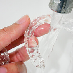 Person rinsing Invisalign aligner under faucet